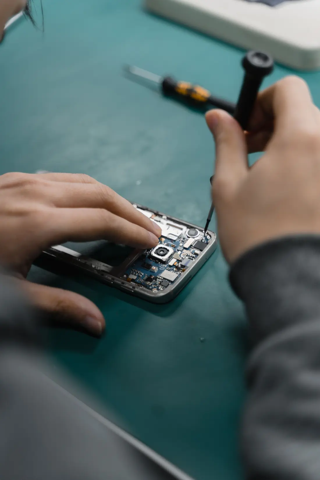 Mãos de um técnico a trabalhar na placa de um smartphone aberto com uma chave de precisão