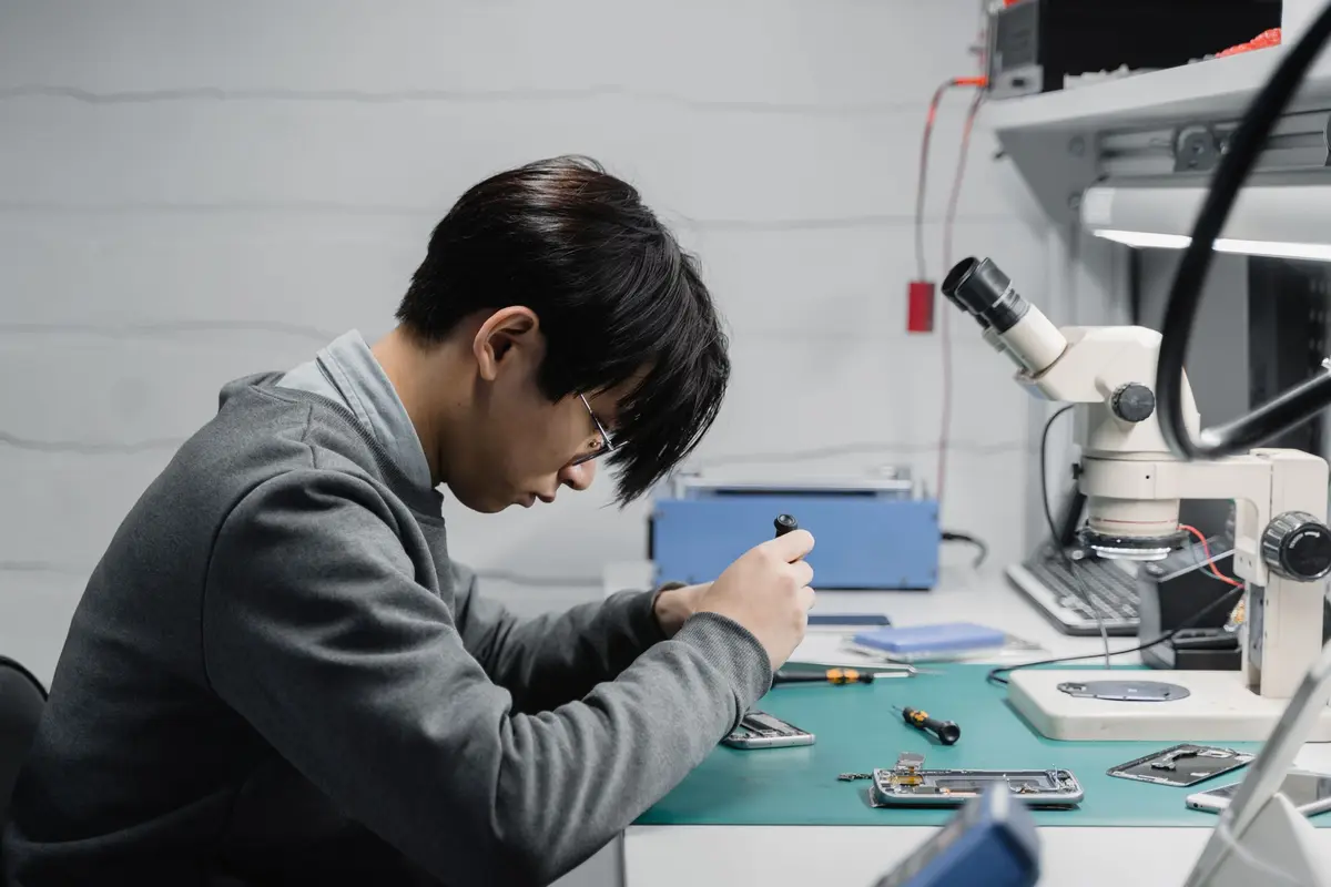 Técnico concentrado a reparar um smartphone na bancada, com microscópio ao lado